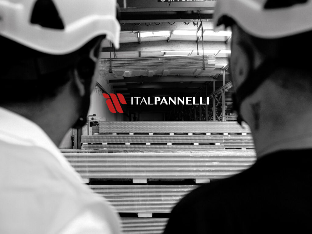 Due uomini di spalle con i caschi da lavoro rivolti verso i pannelli sandwich. Al centro il logo ItalPannelli in sovrimpressione.